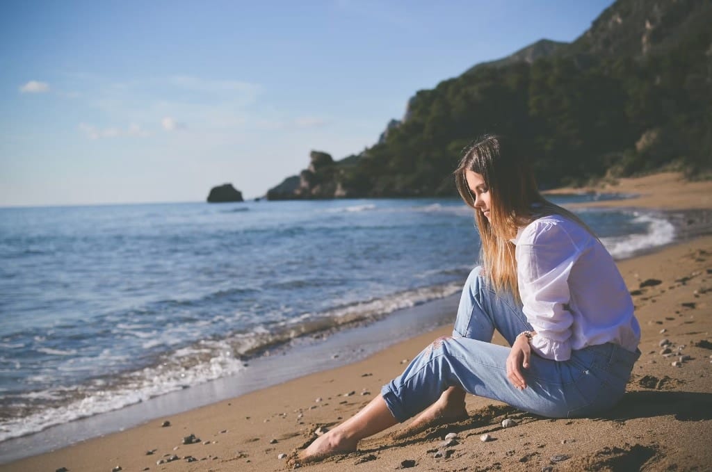 A visitor sitting on the sand looking out to sea at Glyfada Beach, Corfu